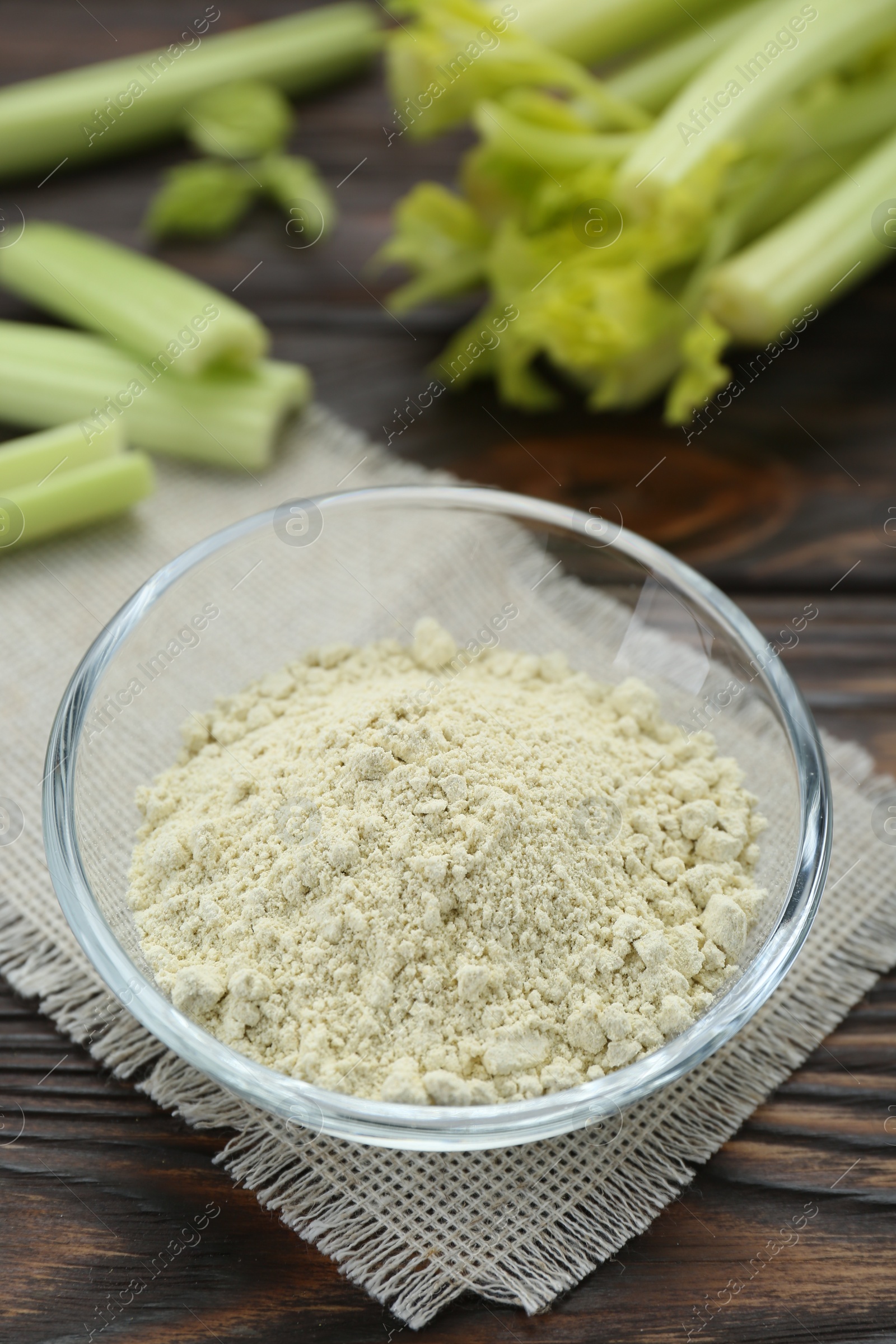 Photo of Natural celery powder in bowl and fresh stalks on wooden table