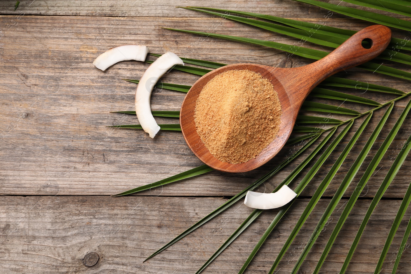 Photo of Spoon with coconut sugar, slices of fruit and palm leaves on wooden table, flat lay. Space for text