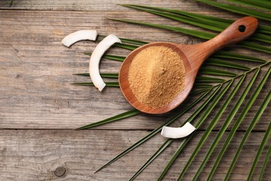 Photo of Spoon with coconut sugar, slices of fruit and palm leaves on wooden table, flat lay. Space for text