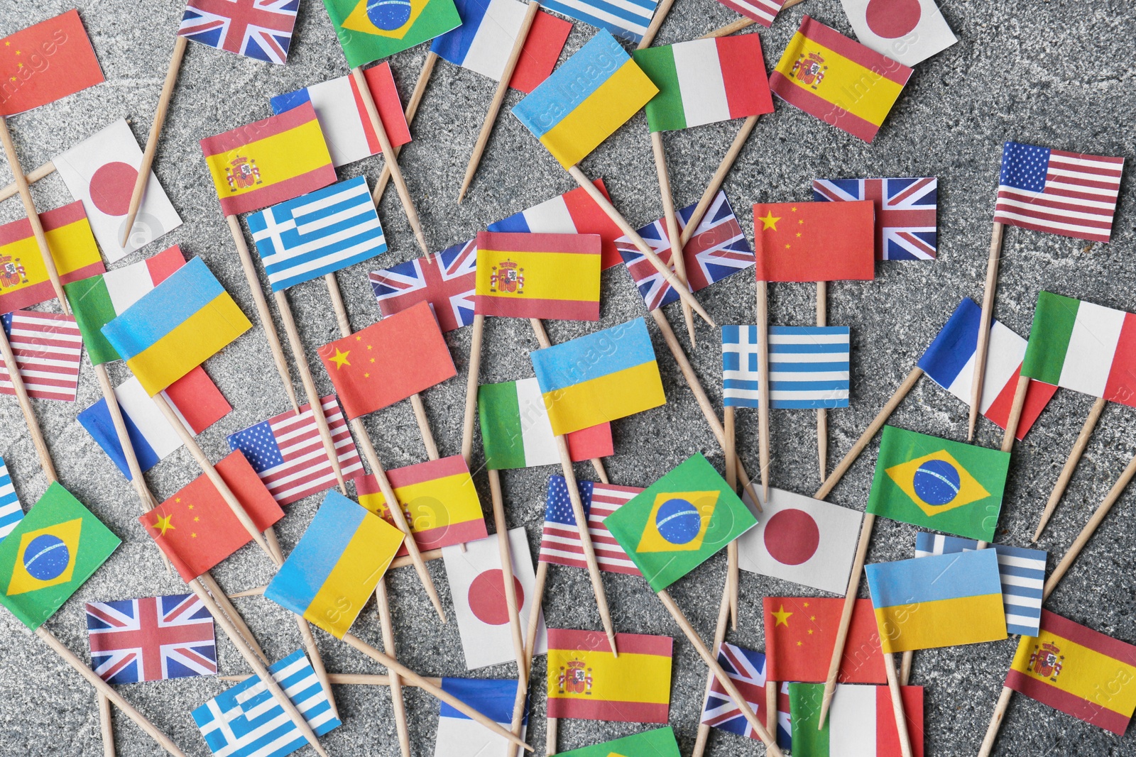Photo of Many small paper flags of different countries on grey table, flat lay
