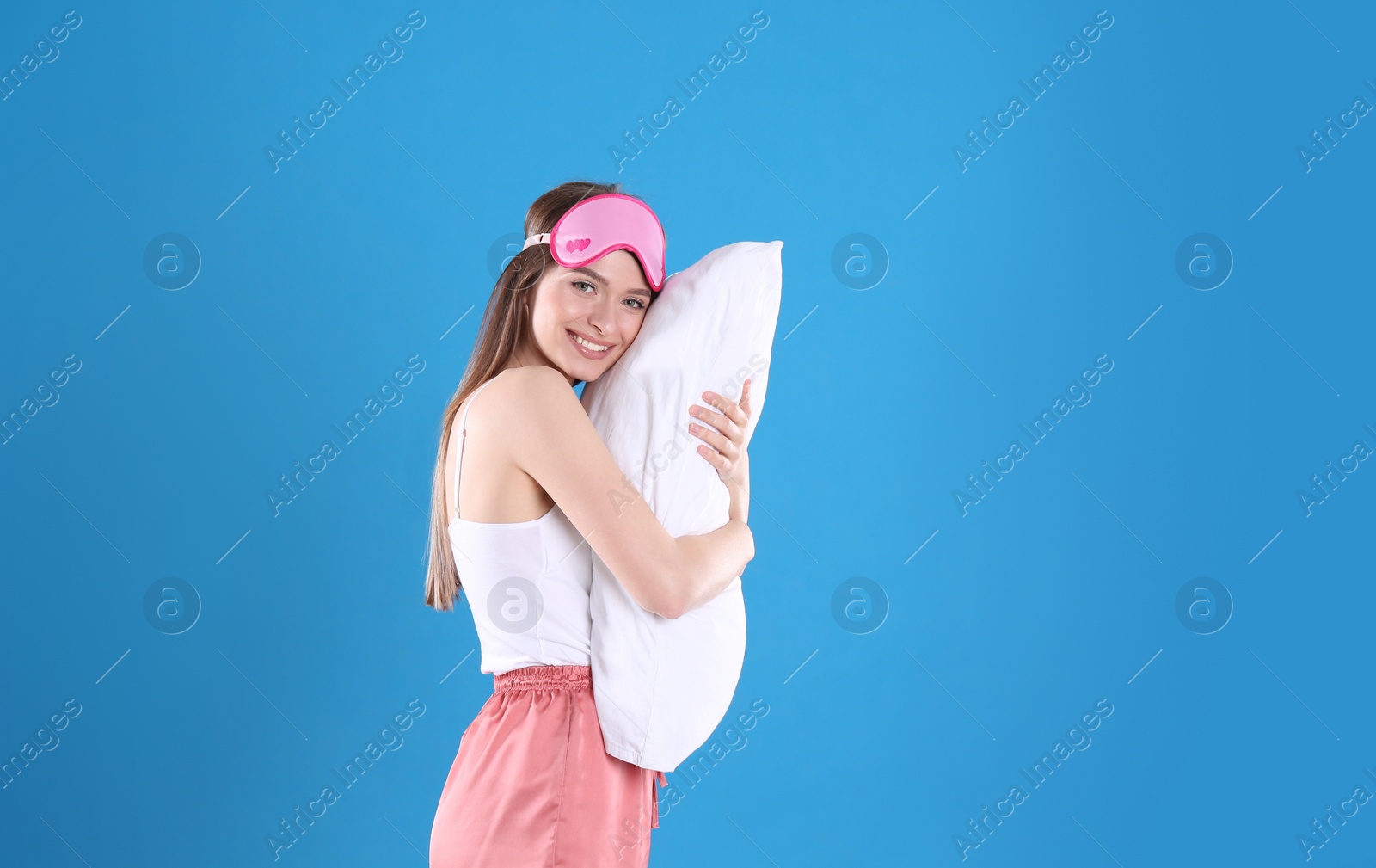 Photo of Young woman with pillow and sleep mask on blue background