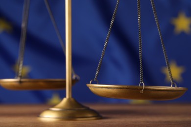 Photo of Scales of justice on wooden table against European Union flag, closeup