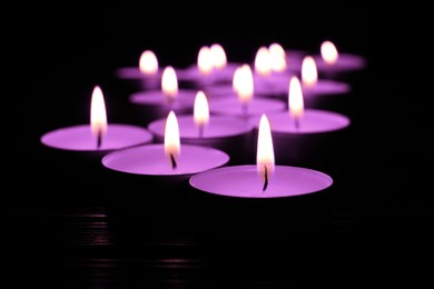 Beautiful burning violet candles on black background, closeup. Funeral attributes