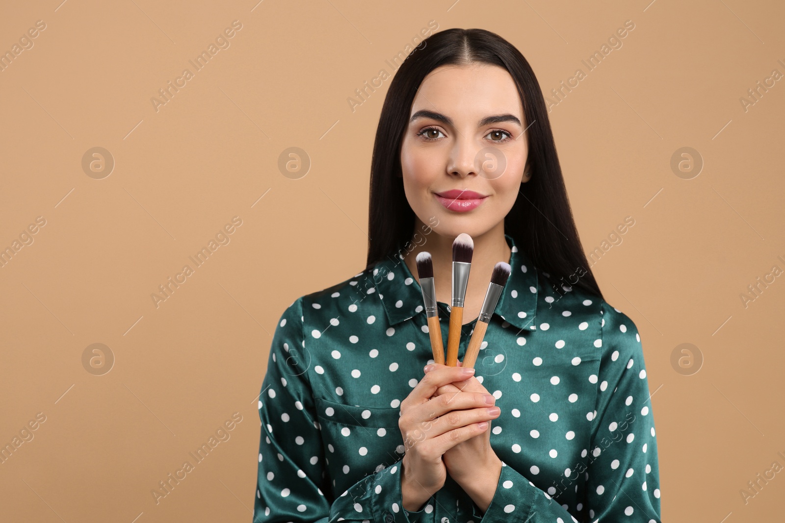 Photo of Beautiful woman with different makeup brushes on light brown background. Space for text