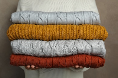 Photo of Woman holding stack of warm clothes on grey background, closeup. Autumn season