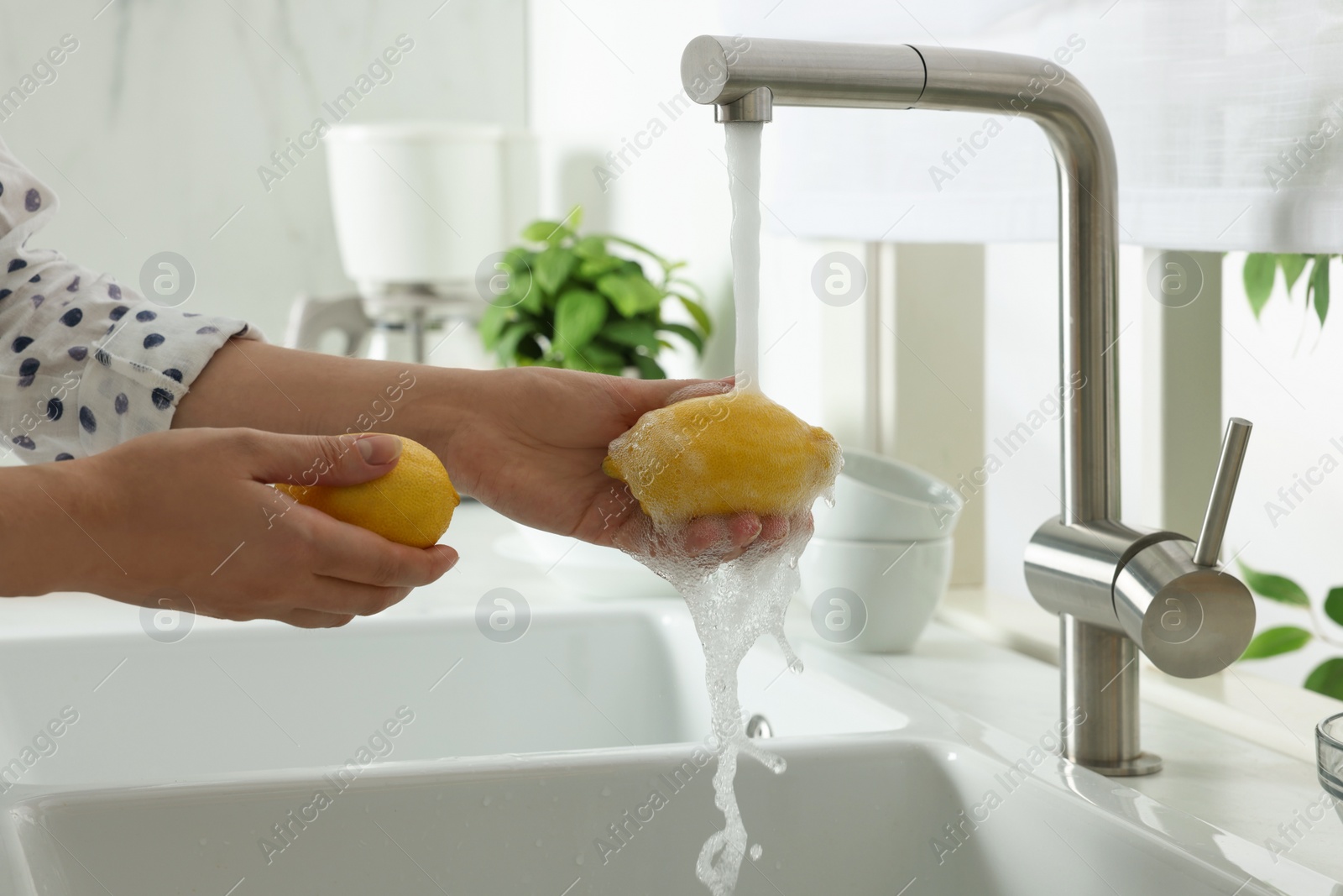 Photo of Woman washing fresh ripe lemons under tap water in kitchen, closeup