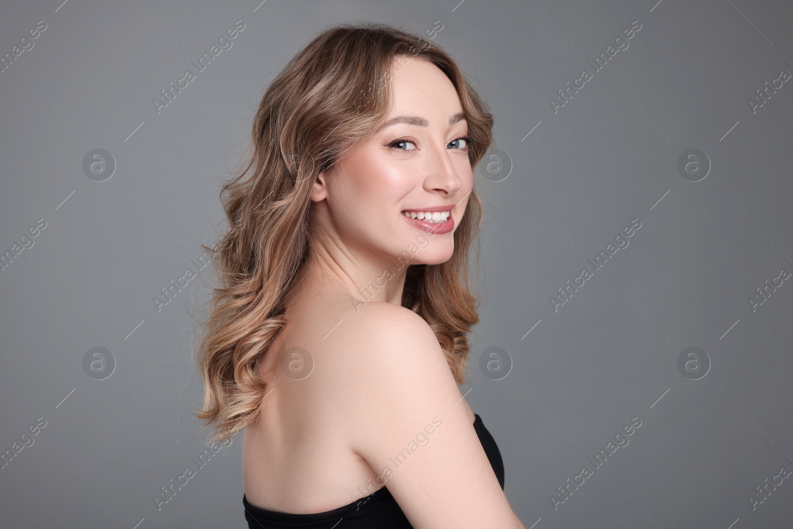 Photo of Portrait of smiling woman with curly hair on grey background