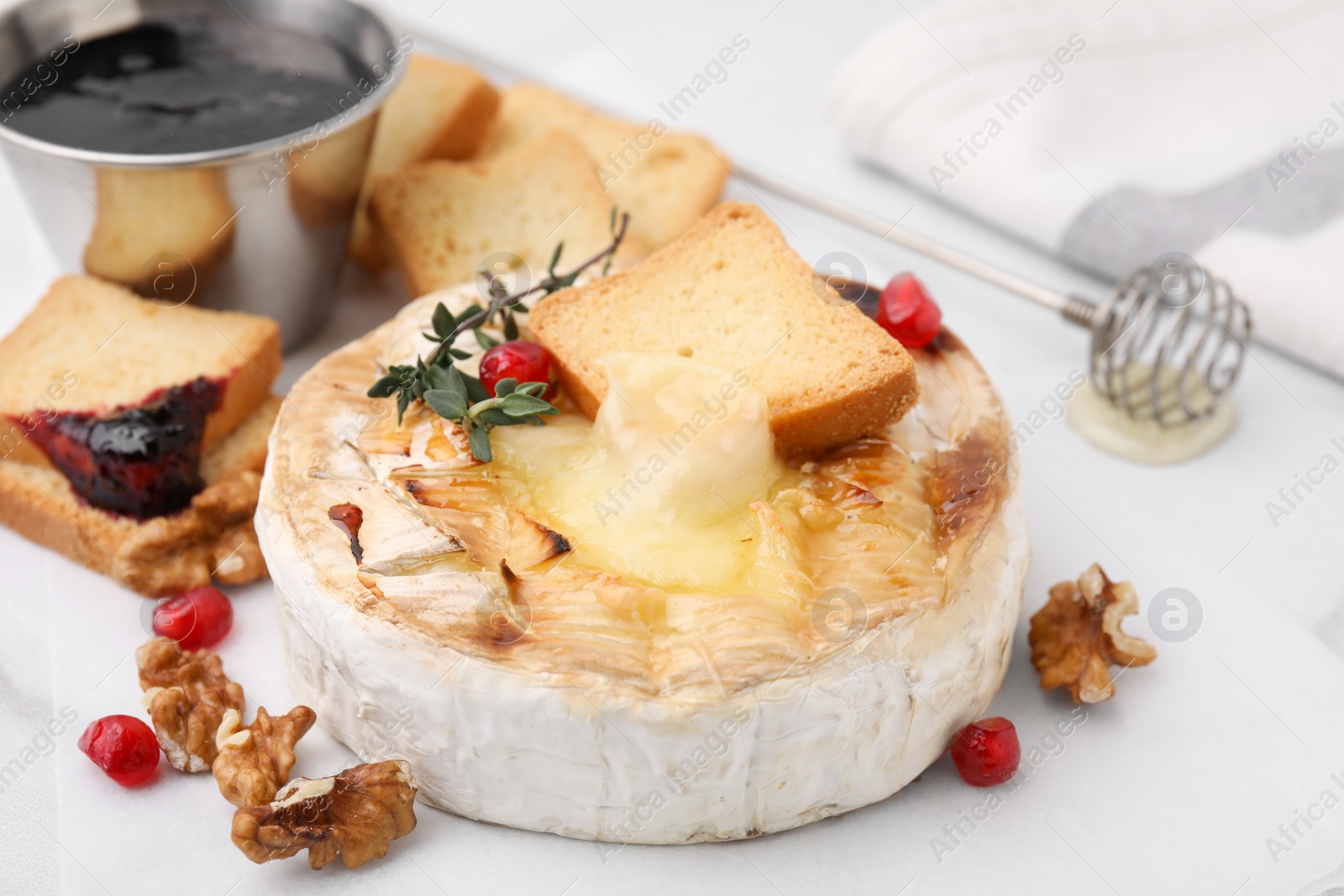Photo of Tasty baked camembert with crouton, thyme, walnuts and pomegranate seeds on white table, closeup