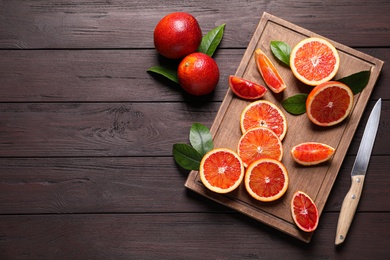 Photo of Whole and cut red oranges on wooden table, flat lay. Space for text