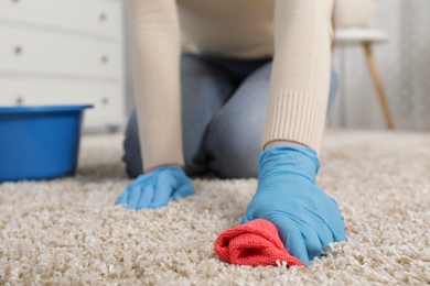 Photo of Woman in rubber gloves cleaning carpet with rag indoors, closeup. Space for text