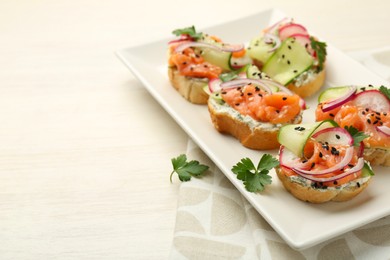 Photo of Tasty canapes with salmon served on white wooden table, closeup. Space for text