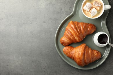 Photo of Tasty croissants served with cup of hot drink on grey textured table, top view. Space for text