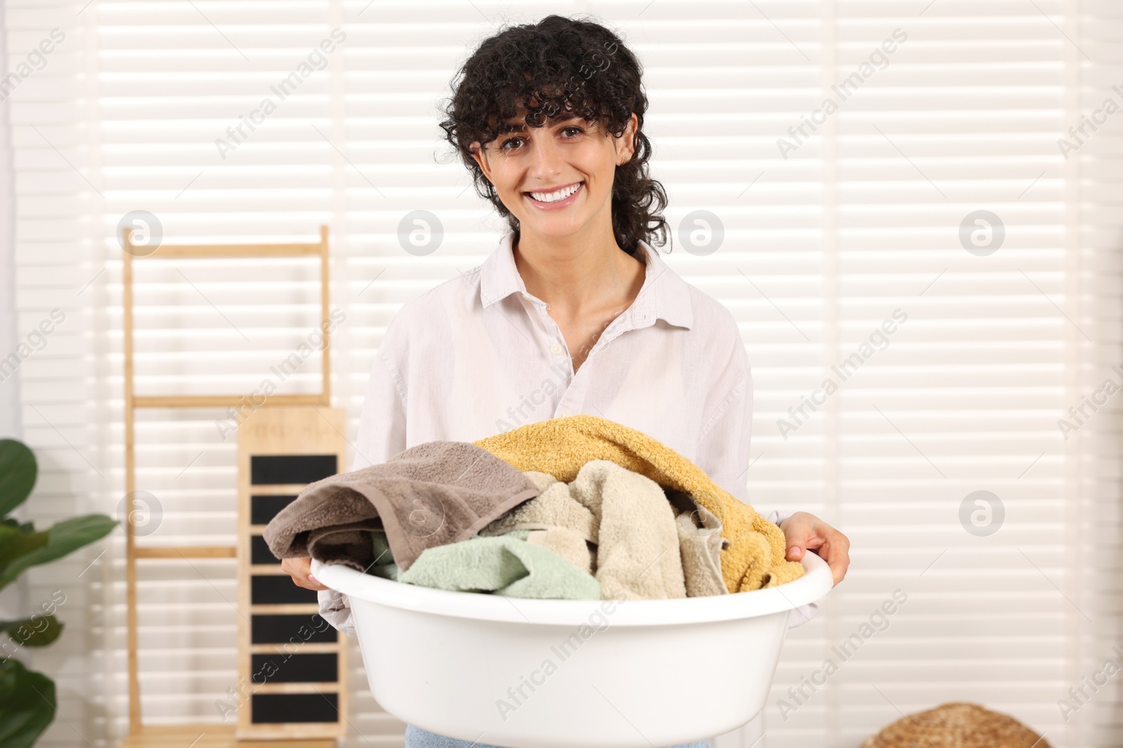 Photo of Happy woman holding basin with laundry indoors