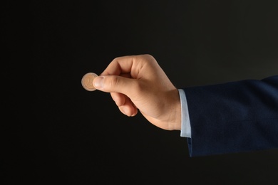 Young man holding coin on black background, closeup