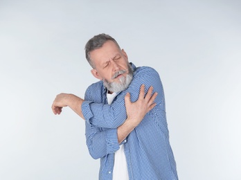 Man suffering from arm pain on light background