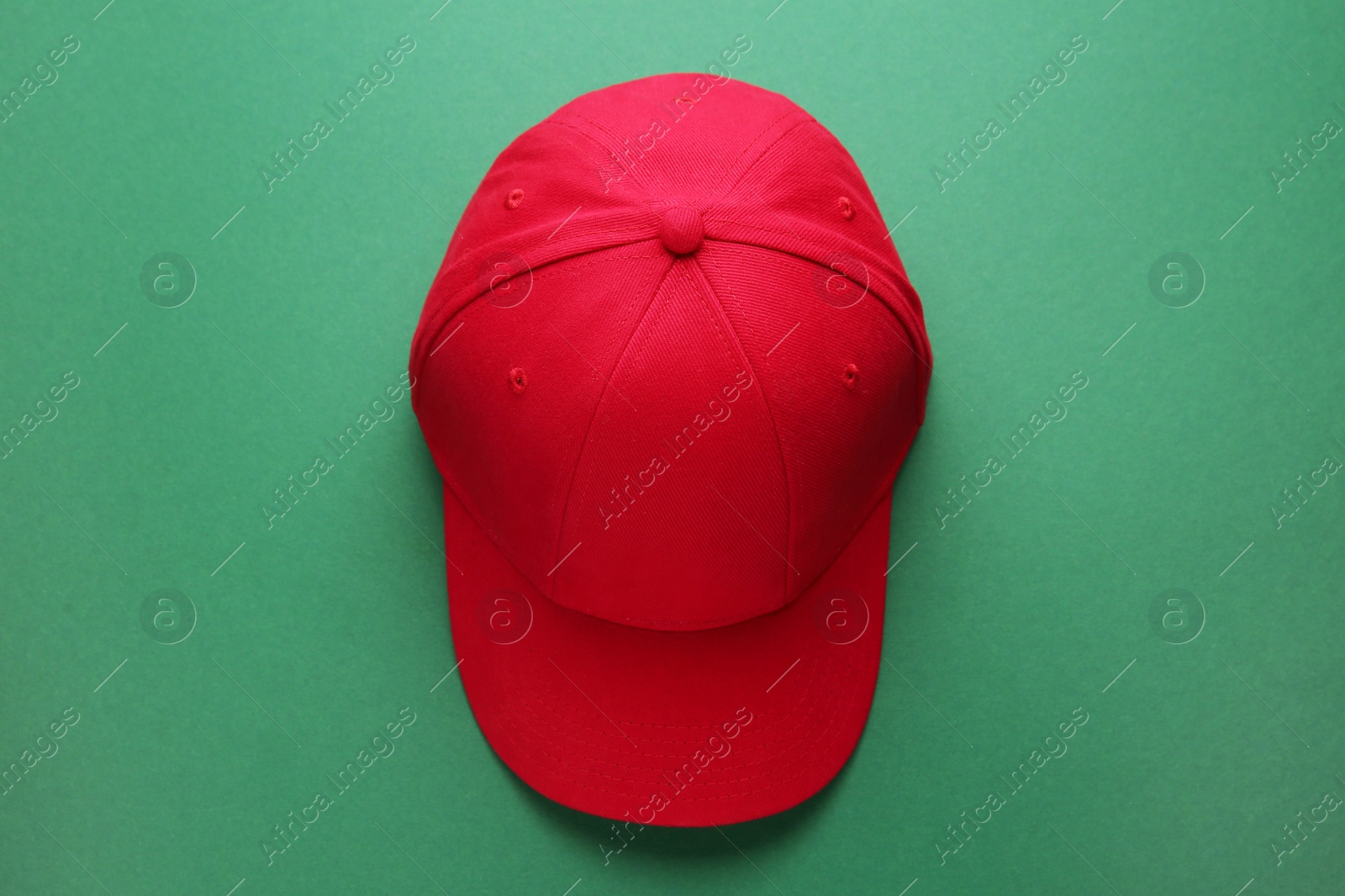 Photo of Stylish red baseball cap on green background, top view