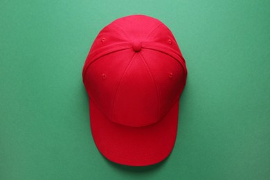 Photo of Stylish red baseball cap on green background, top view