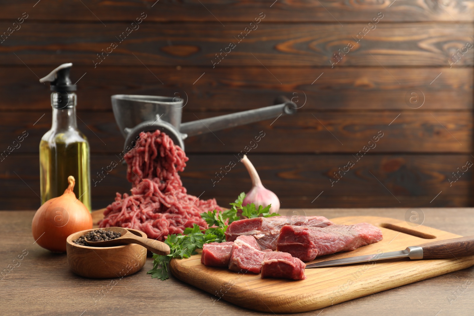 Photo of Manual meat grinder with beef, garlic, onion, parsley, oil and peppercorns on wooden table, space for text