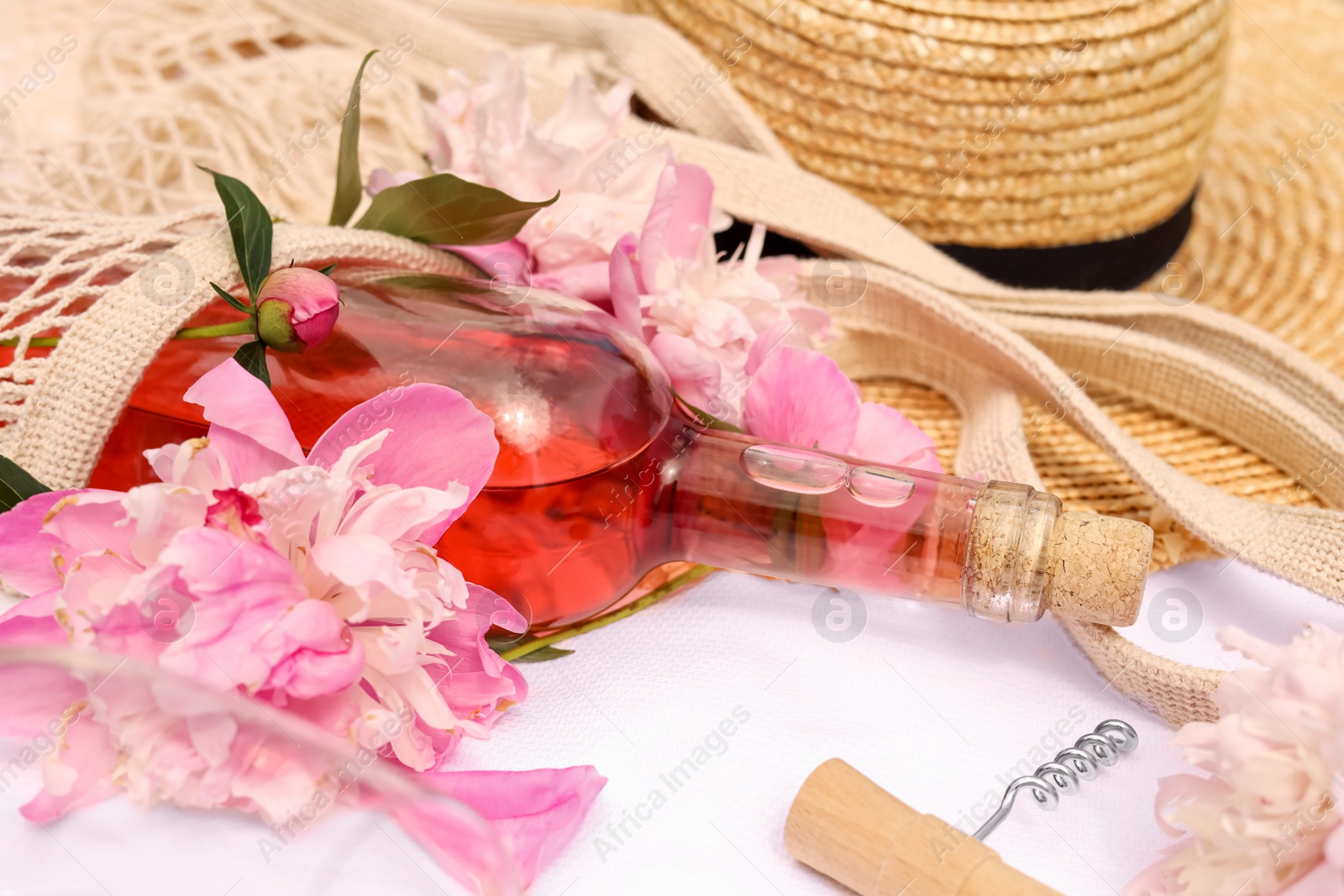 Photo of Bottle of rose wine and peonies on white fabric, closeup