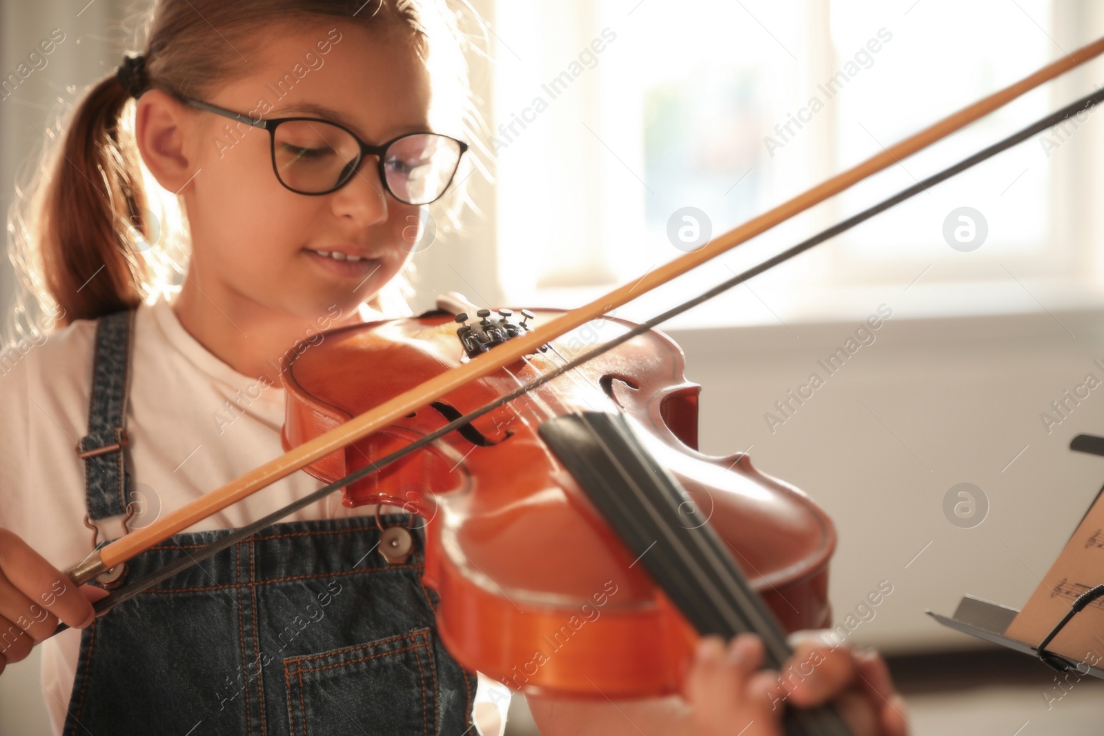 Photo of Cute little girl playing violin indoors, closeup. Music lesson