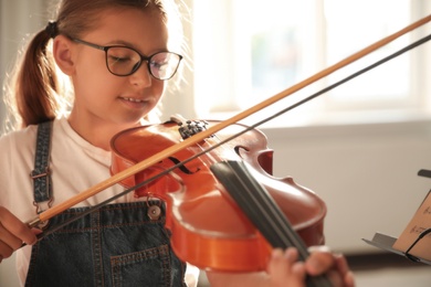 Photo of Cute little girl playing violin indoors, closeup. Music lesson