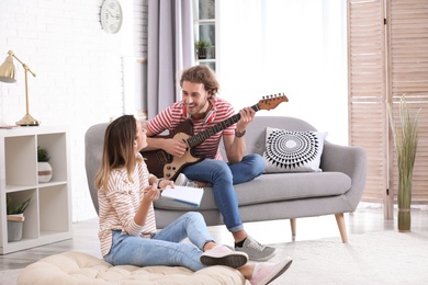Photo of Young man with electric guitar and his girlfriend composing song in living room