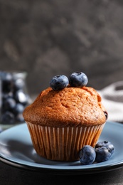 Photo of Plate with tasty muffin and blueberries on grey table, closeup