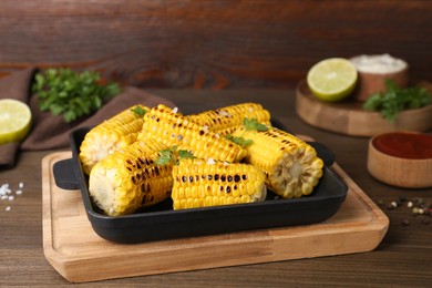 Photo of Tasty grilled corn and ingredients on wooden table