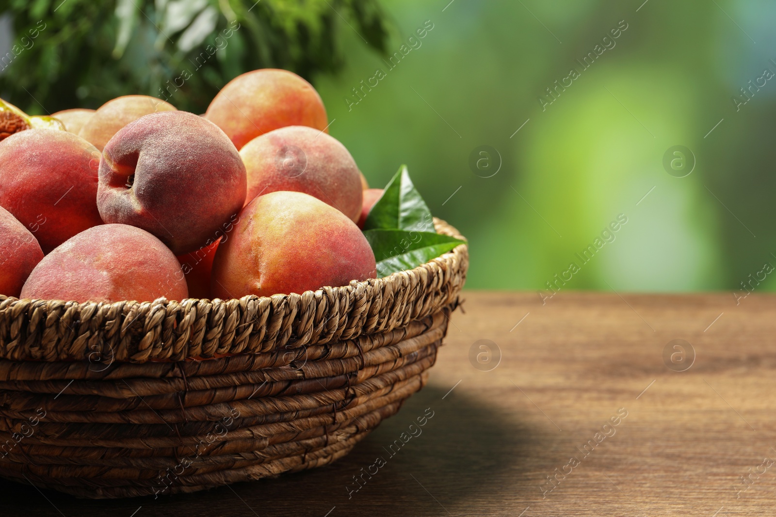 Photo of Many whole fresh ripe peaches in basket on wooden table against blurred background, closeup. Space for text