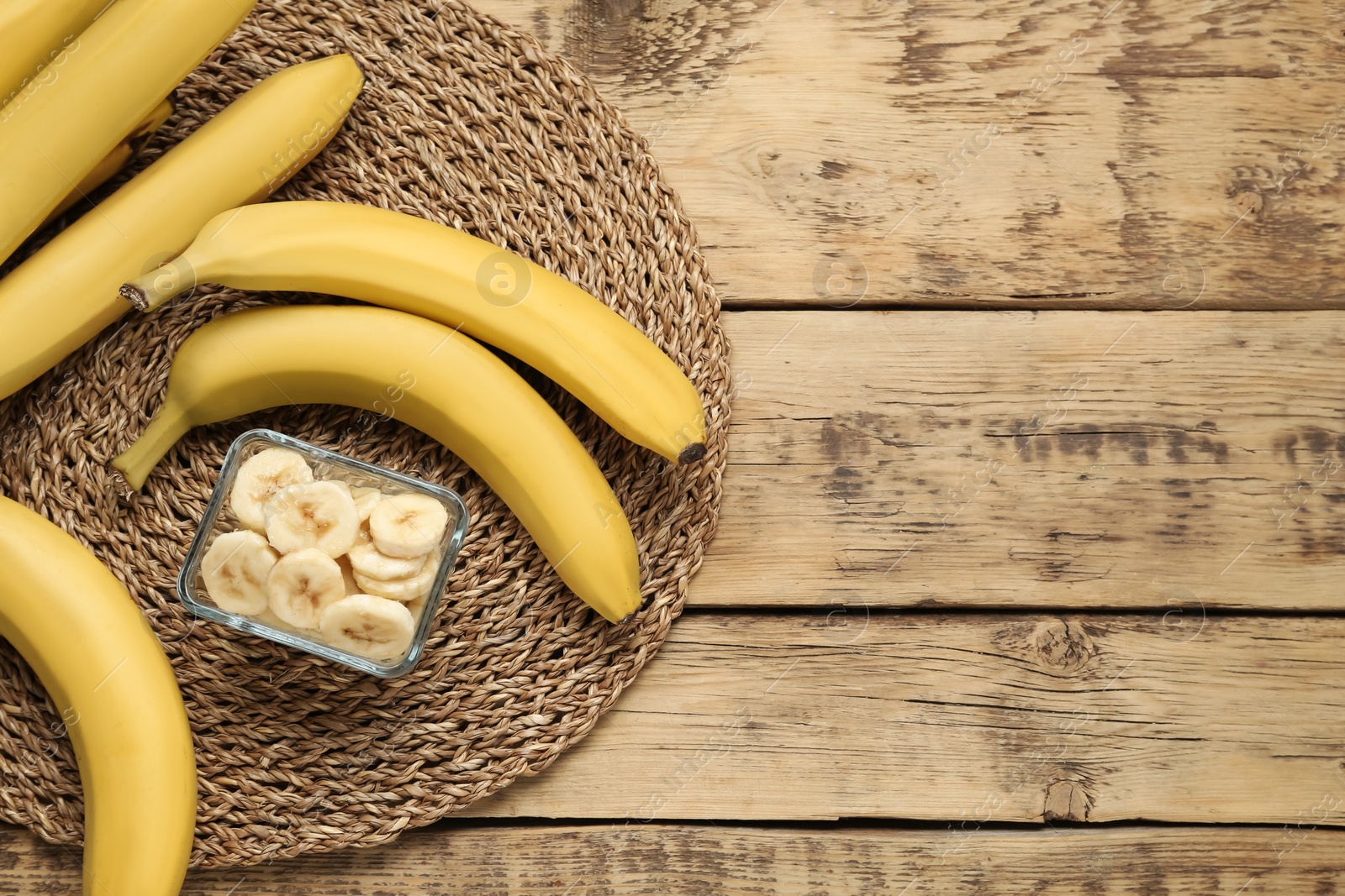 Photo of Bowl with cut bananas near whole fruits on wooden table, flat lay. Space for text