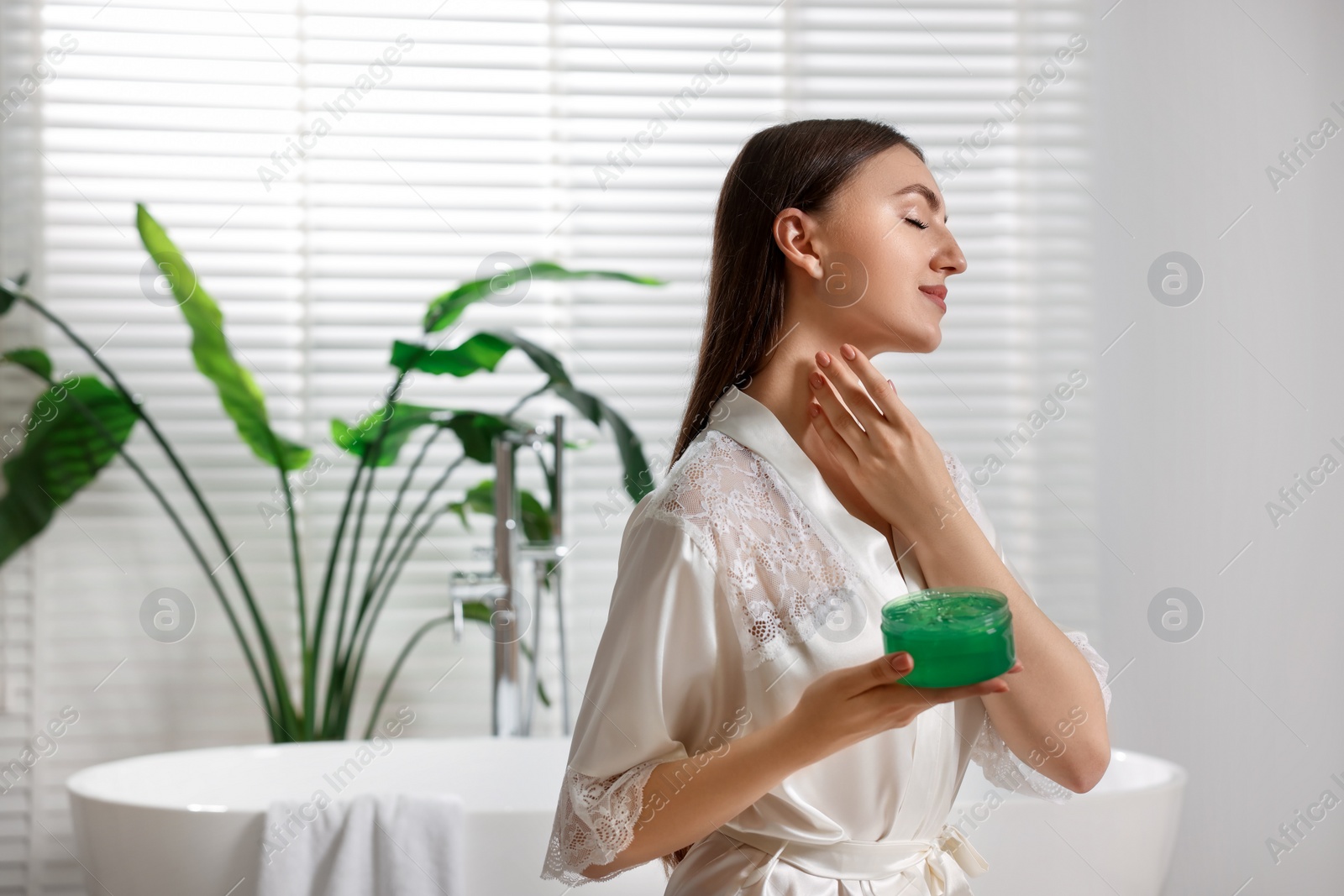 Photo of Young woman applying aloe gel onto her neck in bathroom. Space for text