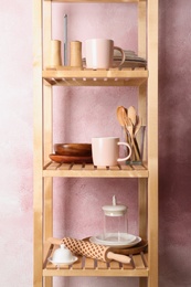 Photo of Wooden shelving unit with set of kitchenware near color wall