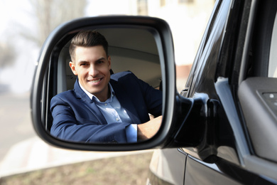 Photo of Handsome man looking into side view mirror of modern car outdoors