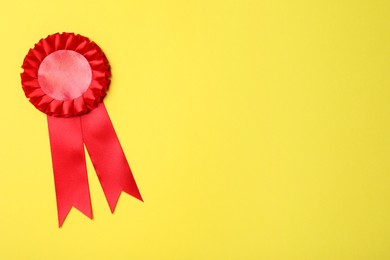 Photo of Red award ribbon on yellow background, top view. Space for text