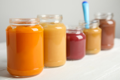 Healthy baby food in jars on white wooden table