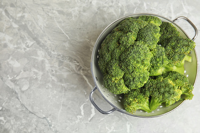 Photo of Fresh green broccoli in colander on grey marble table, top view. Space for text