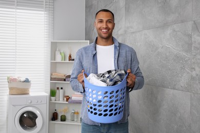Photo of Happy man with basket full of laundry in bathroom
