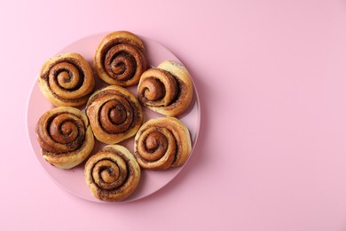 Photo of Many tasty cinnamon rolls pink background, top view. Space for text