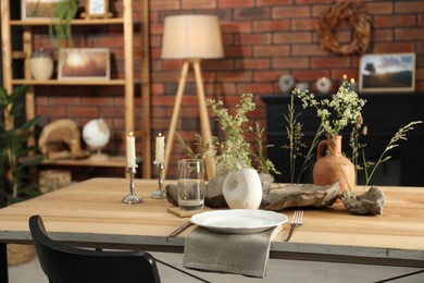 Photo of Set of clean dishware, vases with beautiful flowers, stones and burning candles on wooden table in stylish dining room