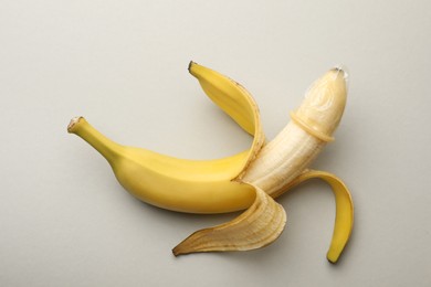 Photo of Banana with condom on light grey background, top view. Safe sex concept