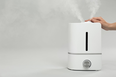 Photo of Woman using modern air humidifier on light grey background, closeup. Space for text