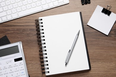 Open blank notebook, keyboard and stationery on wooden table, flat lay