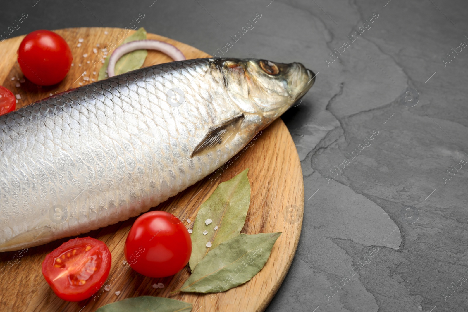 Photo of Tray with salted herring, onion, bay leaves and cherry tomatoes on black table, closeup. Space for text