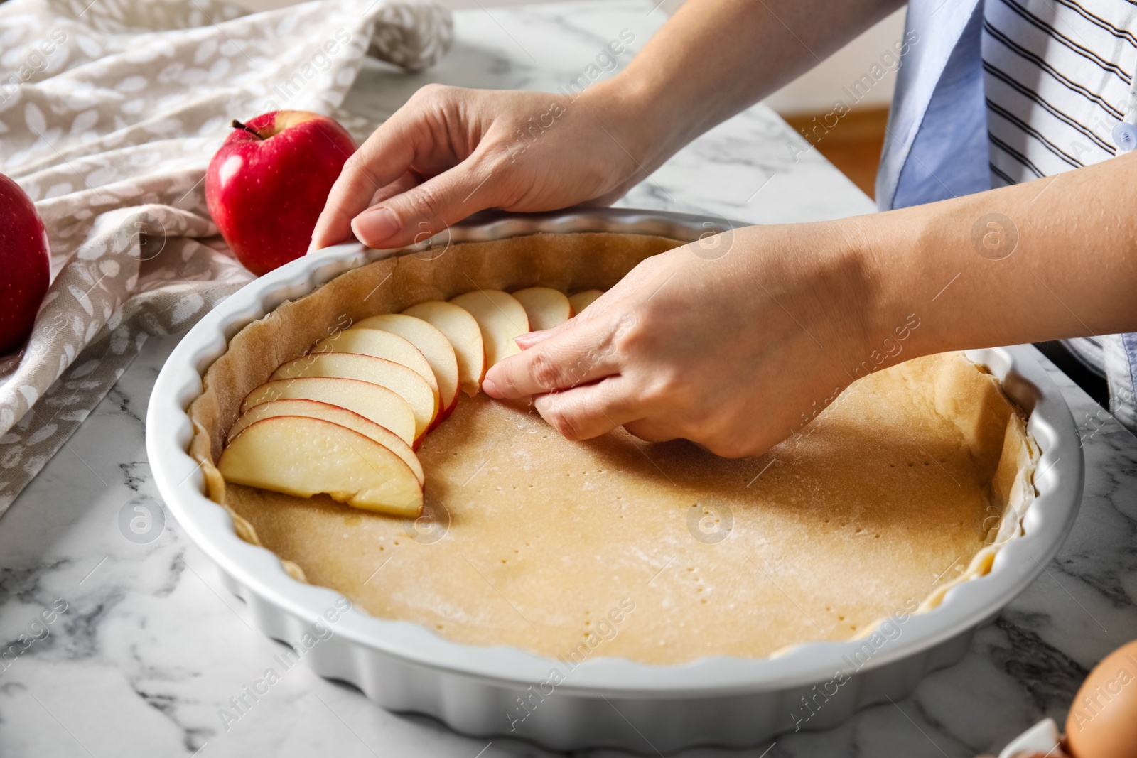 Photo of Woman putting apple slice into baking dish with dough to make traditional English pie at white marble table, closeup