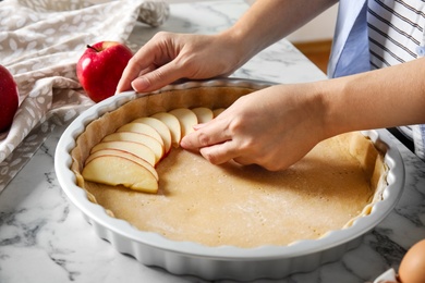 Woman putting apple slice into baking dish with dough to make traditional English pie at white marble table, closeup