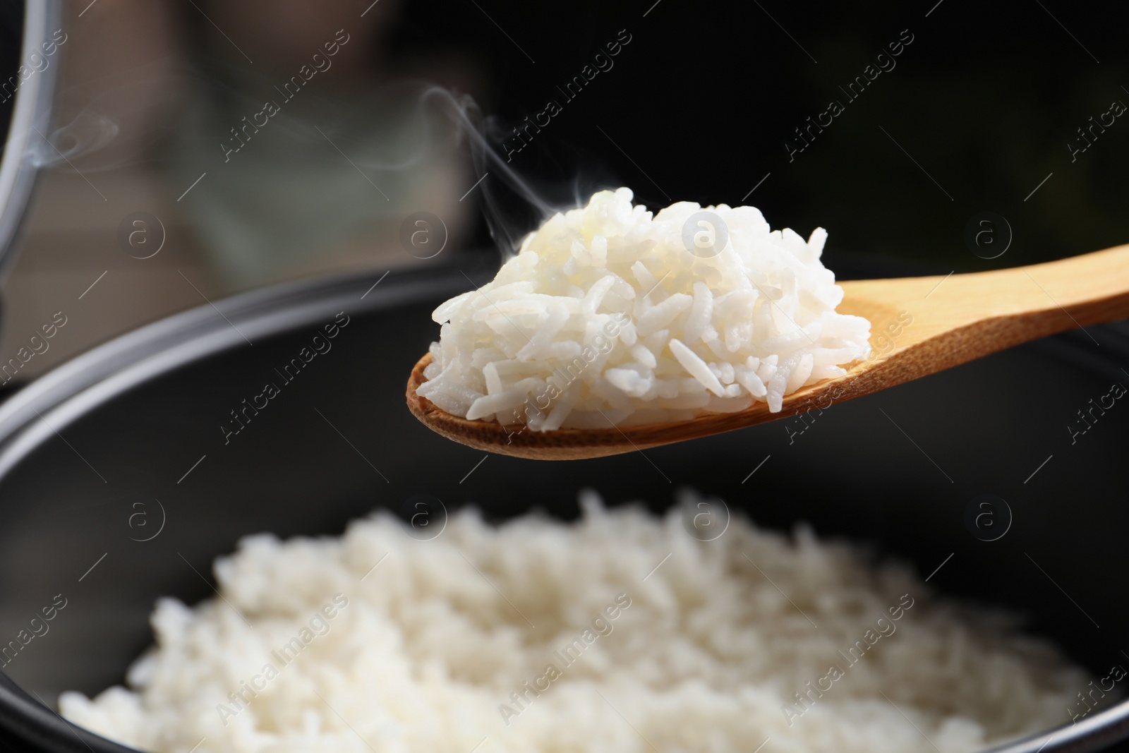 Photo of Spoon with tasty hot rice over cooker, closeup