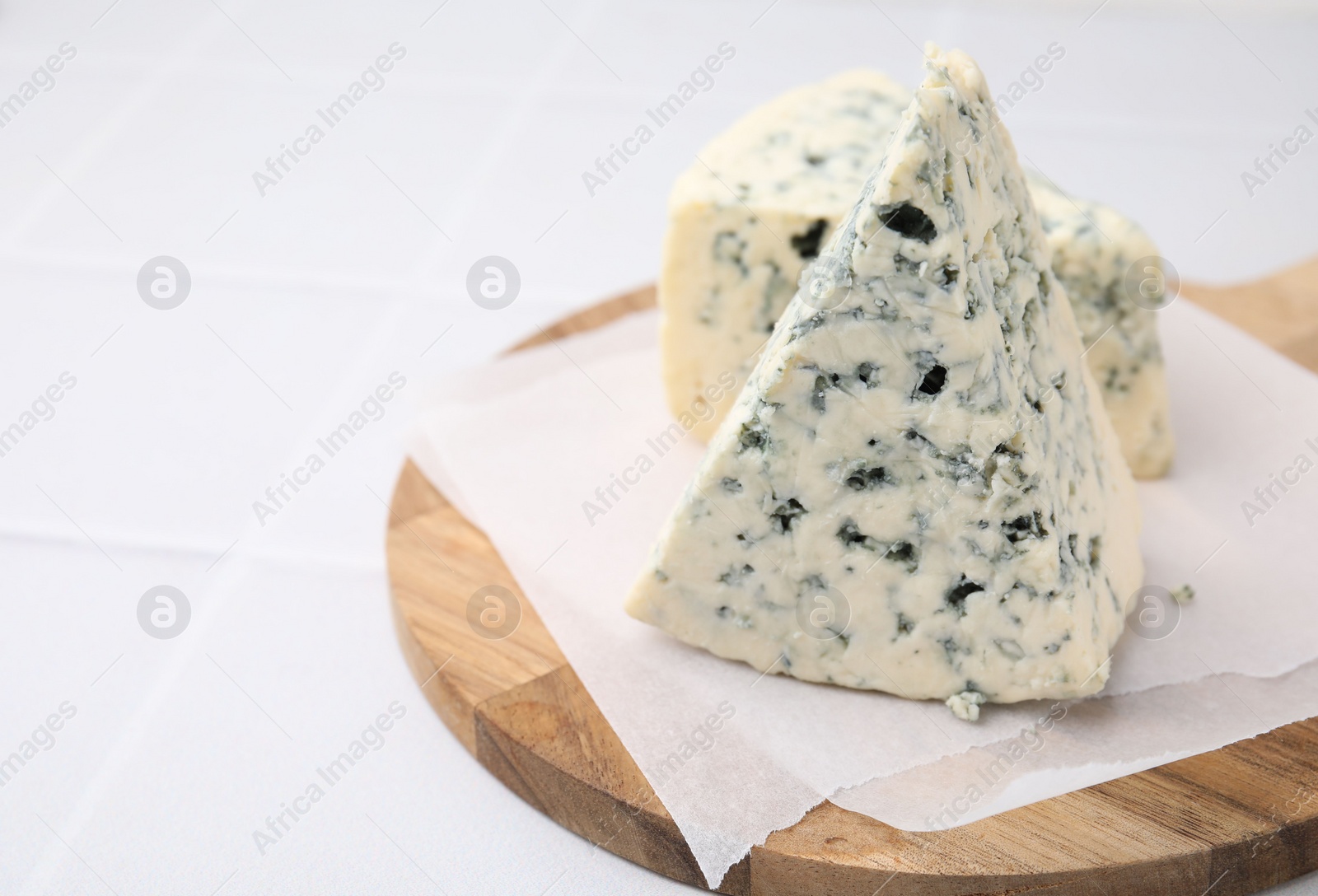 Photo of Wooden cutting board with blue cheese on white tiled table, closeup. Space for text