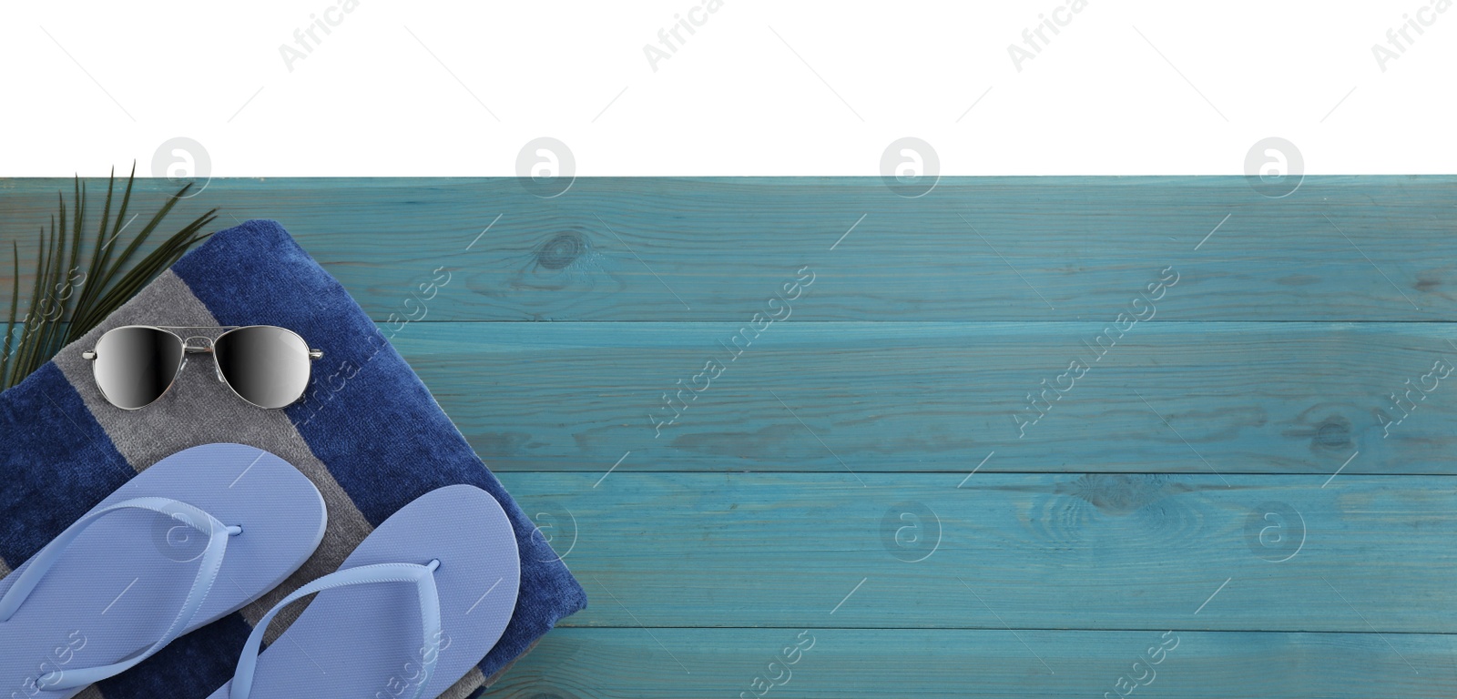 Photo of Light blue wooden surface with beach towel, sunglasses and flip flops on white background, top view. Space for text
