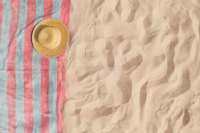 Towel with straw hat on sandy beach, top view. Space for text