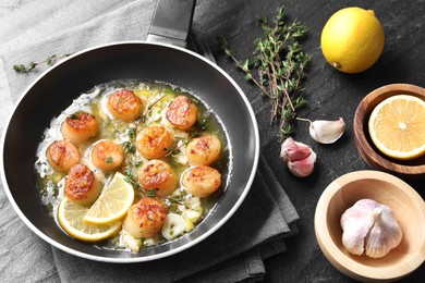Photo of Delicious scallops with sauce in frying pan and ingredients on dark gray textured table, above view